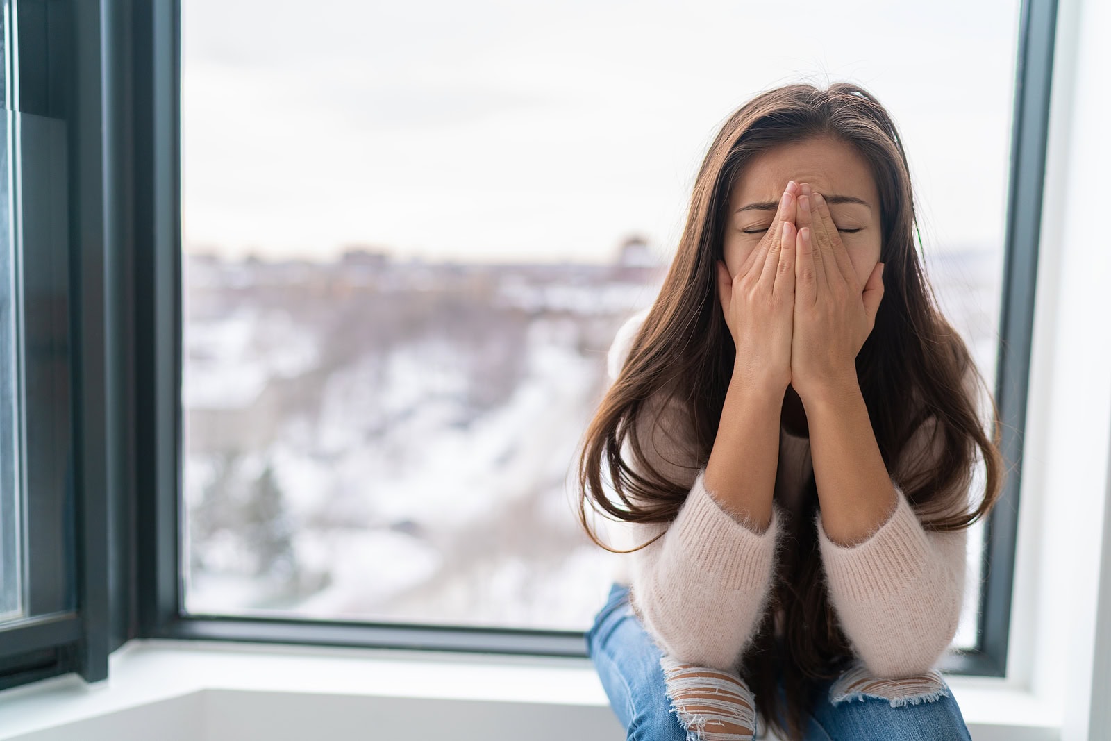 Drying woman's face with hands indoors during winter cold weather, seeking comfort and warmth.