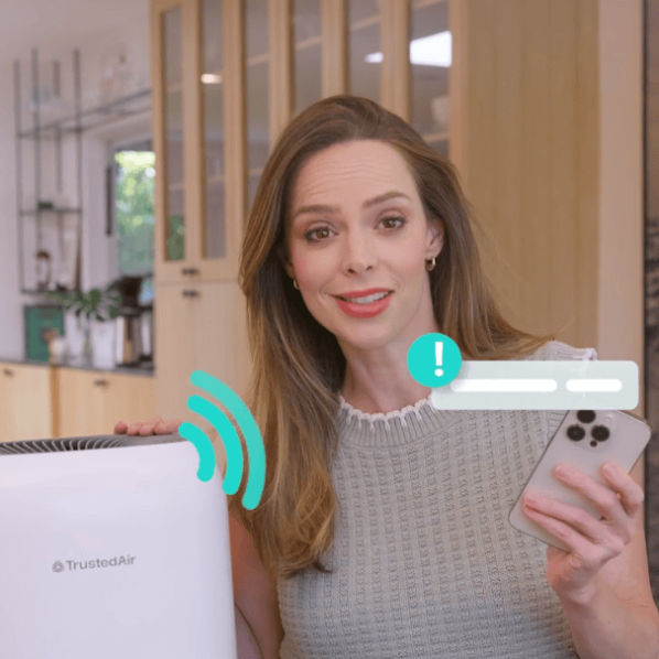 Woman using TrustedAir air quality monitor with smartphone in modern home, demonstrating smart indoor air quality management.
