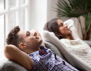 Relaxing couple resting on sofa with refreshed air, enjoying clean, quality indoor air for better sleep and comfort.