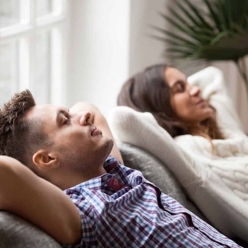 Relaxing couple resting on sofa with refreshed air, enjoying clean, quality indoor air for better sleep and comfort.