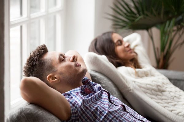 Relaxed couple resting on a sofa near a window, enjoying a peaceful moment indoors.