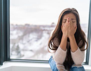 Drying woman's face with hands indoors during winter cold weather, seeking comfort and warmth.