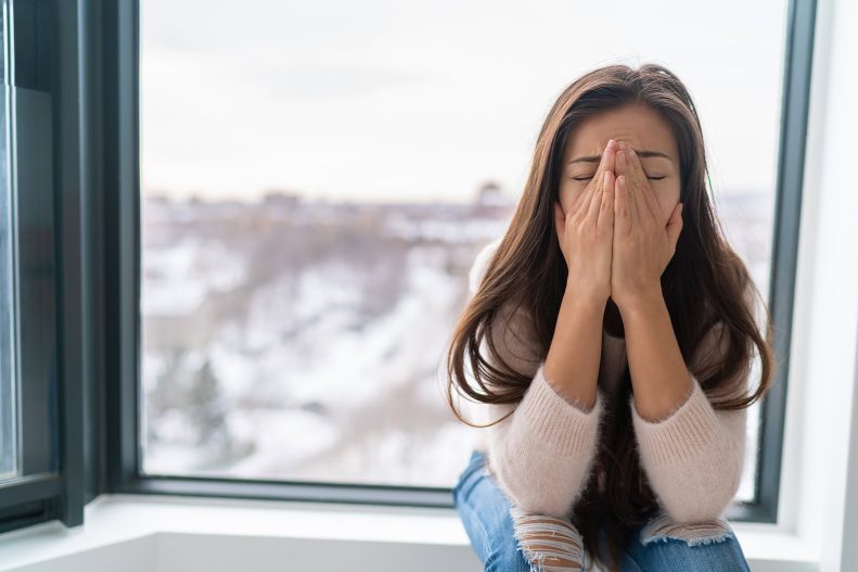 Drying woman's face with hands indoors during winter cold weather, seeking comfort and warmth.